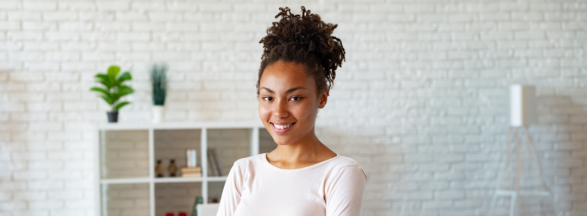 The image is a photograph of a woman with light skin, smiling at the camera. She appears to be in her late twenties or early thirties and has long hair. Her eyes are looking directly at the camera, and she is holding up her index finger near her mouth as if she s making a point or emphasizing something. The background is plain and light-colored, which suggests that this could be a stock photo used for various purposes such as advertising, personal branding, or lifestyle content.