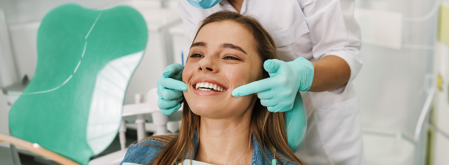 The image shows a woman seated in a dental chair, receiving dental care with a smile on her face, while a dental professional is attending to her with a dental mirror and tools.