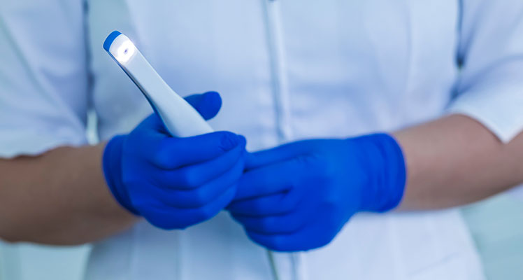 A healthcare professional wearing blue gloves and holding a smartphone with a white flashlight.