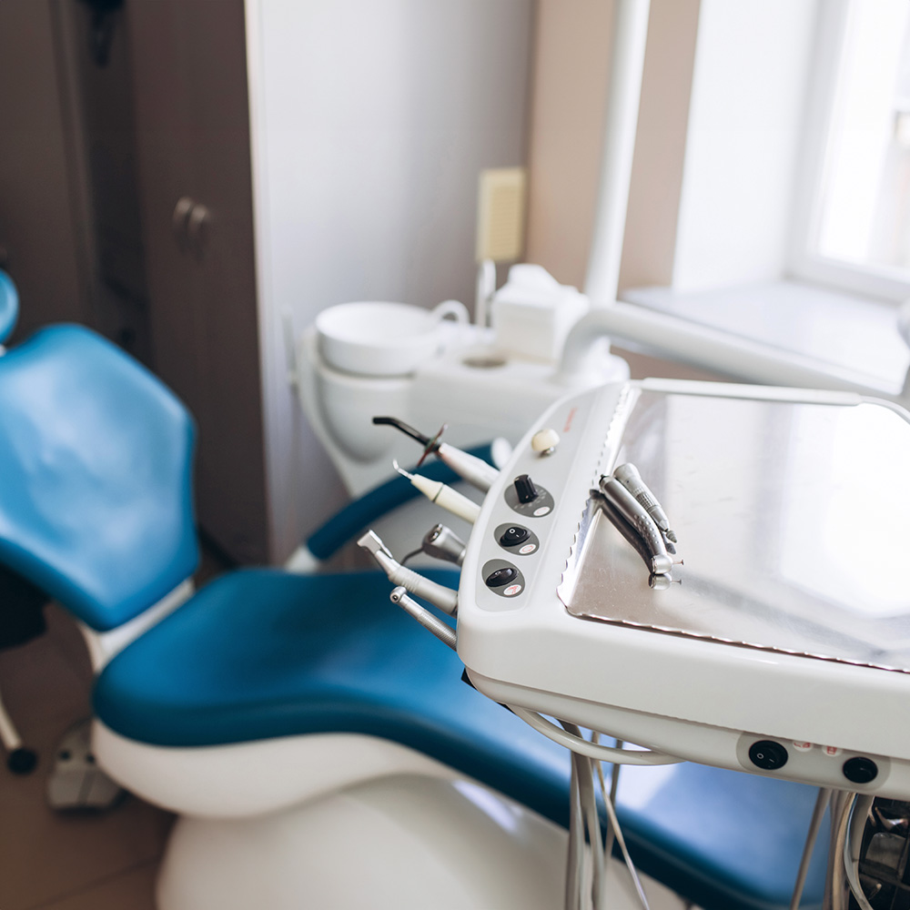 The image shows a dental office interior with a dental chair, examination table, and dental equipment, including a dental mirror and instruments.