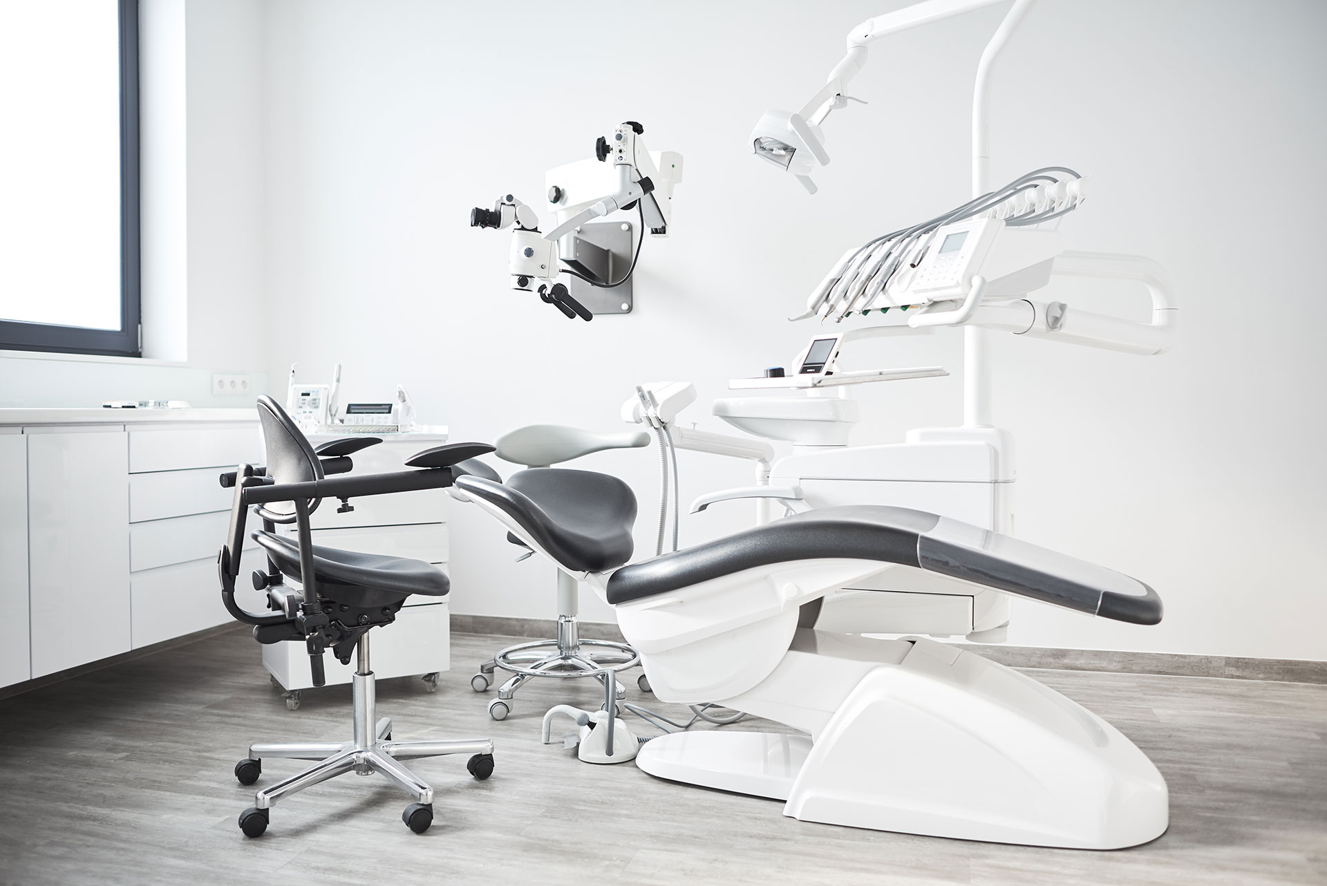 The image shows a modern dental office with various pieces of equipment, including a dental chair, a computerized system, and a large screen displaying an X-ray.