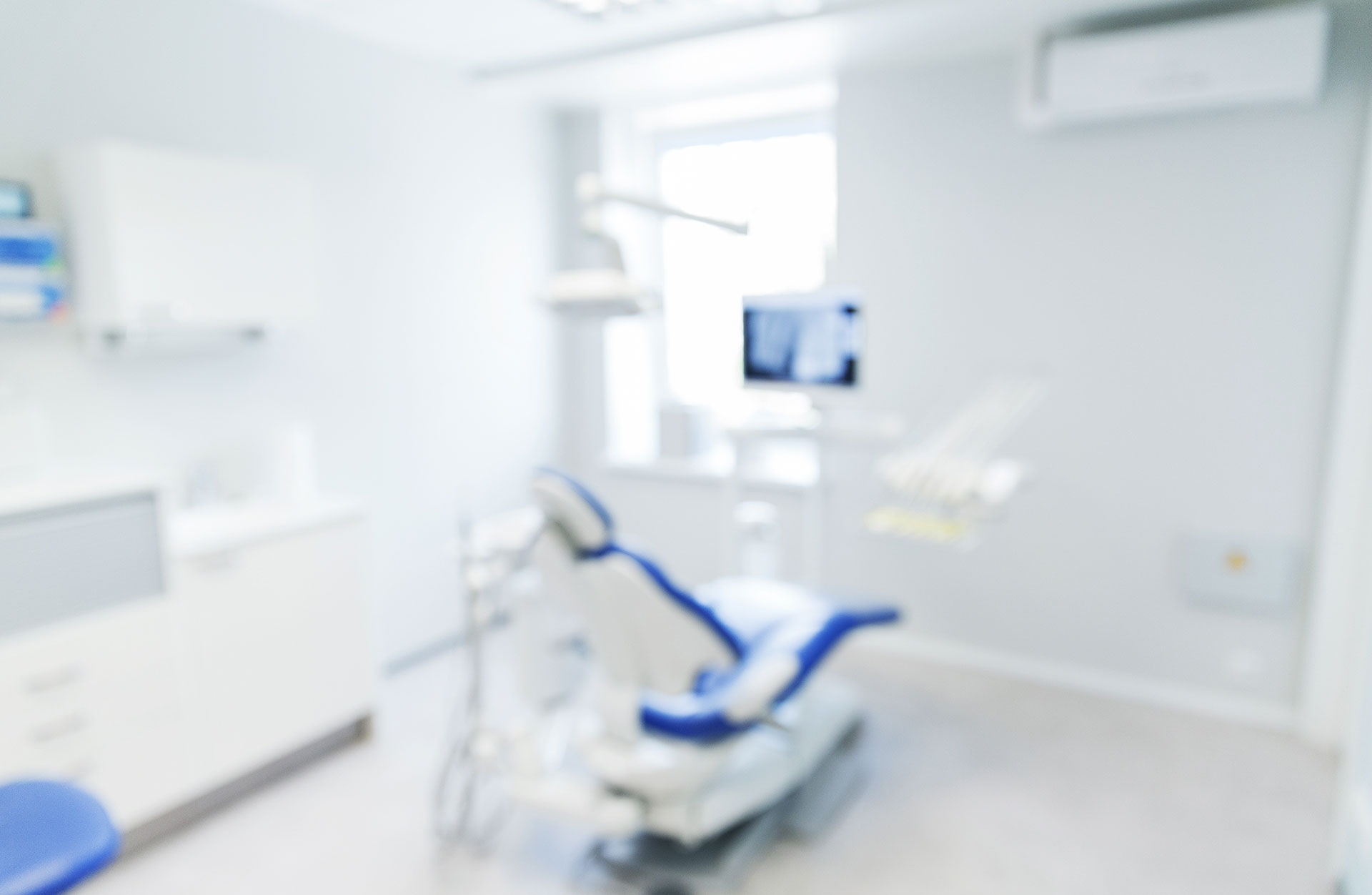 Medical dental chair in a sterile room with equipment and a window.