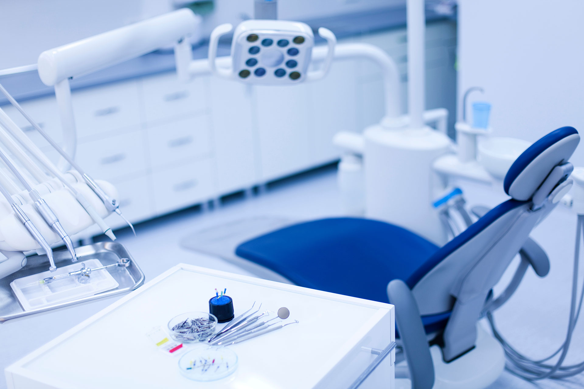 The image depicts a professional dental office with a blue chair, equipment, and a clean environment.