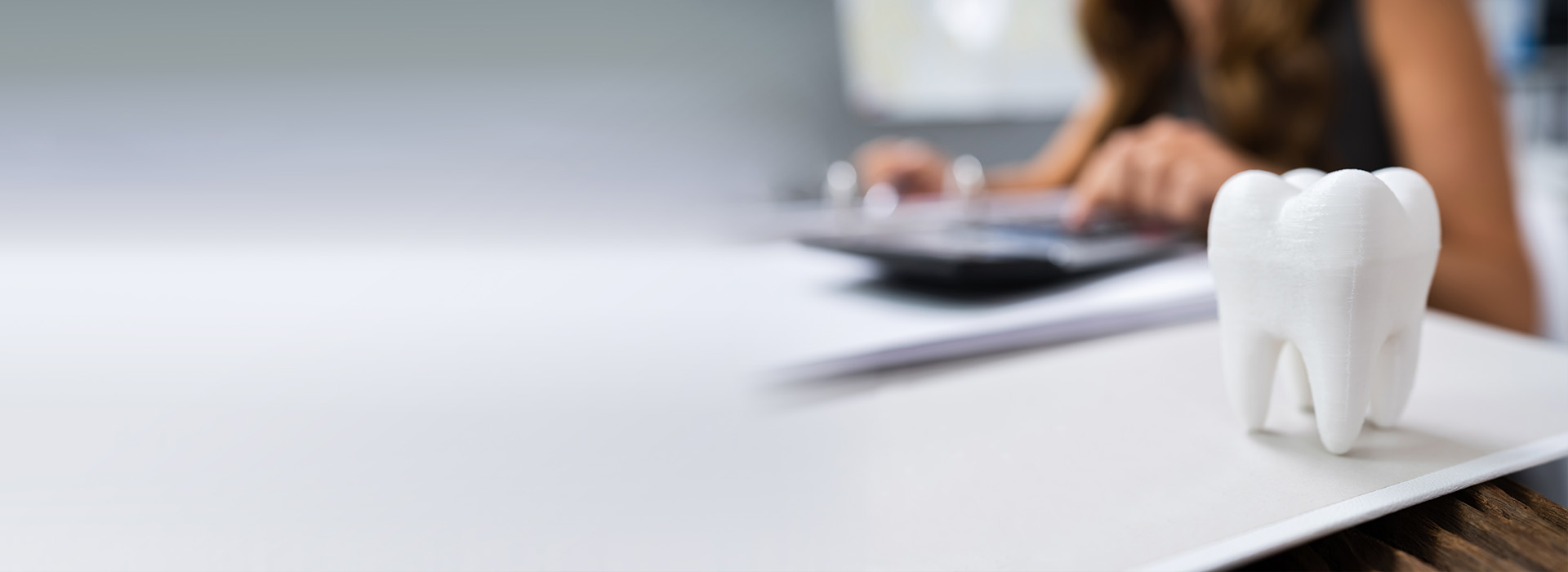 The image shows a person sitting at a desk with a laptop, writing on paper, and a white toothbrush holder in the foreground.