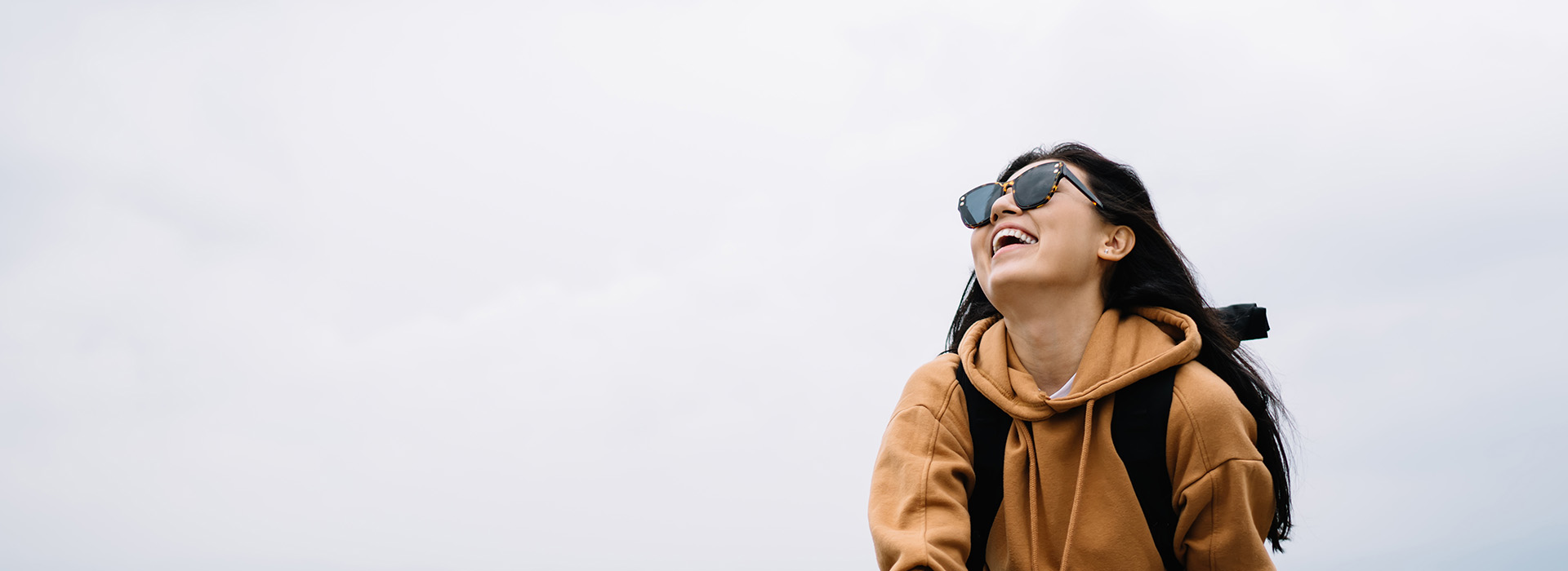 A person in a hoodie with sunglasses, smiling and looking at the camera, set against an overcast sky.