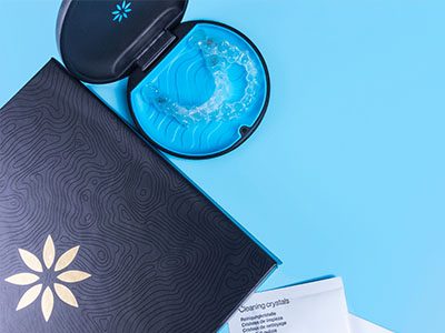 An open blue package containing a dental impression tray with a toothbrush and a pamphlet, against a blue background.