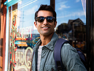 A man with sunglasses, a backpack, and a jacket stands in front of a store window.