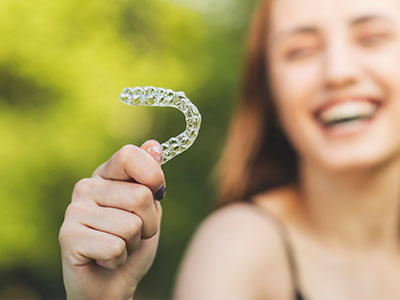 The image shows a person holding up a clear plastic retainer with their hand.