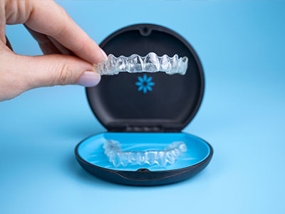 An image of a person s hand holding an open dental retainer case with a blue tray containing clear aligners, showcasing the product for teeth straightening.