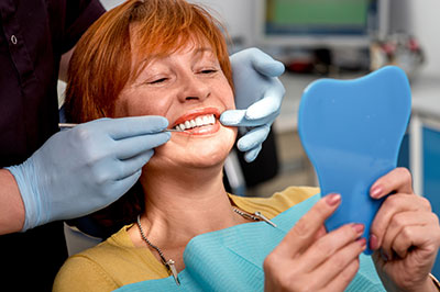 A woman receiving dental care, with a smile on her face, being assisted by a dental professional.