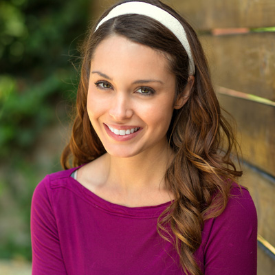 The image features a woman with long hair smiling at the camera, wearing a purple top and a headband.