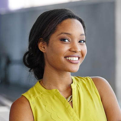 The image features a young woman with a bright smile, wearing a yellow top and standing against a blurred background.