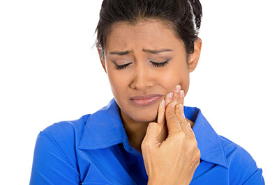 The image shows a woman with her eyes closed, holding her face and looking distressed while standing in front of a blue background.