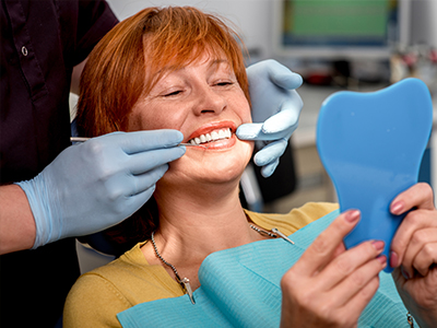 A woman with red hair is sitting in a dental chair, receiving a dental treatment, with a blue mouthguard on her teeth.