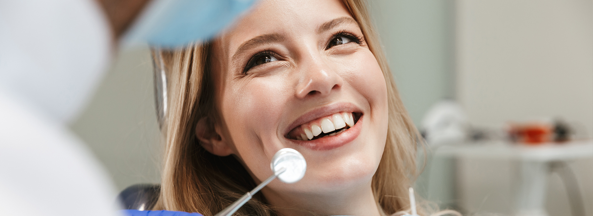 The image shows a woman with a bright smile, sitting in front of a medical professional who appears to be examining her.