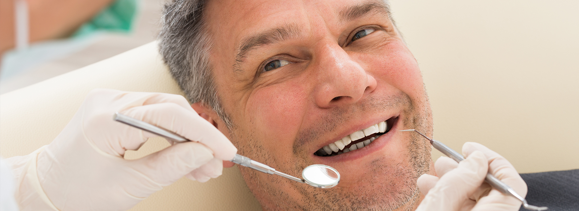 The image shows a man in a dental chair receiving dental care, with a smile on his face and a dentist working on him.