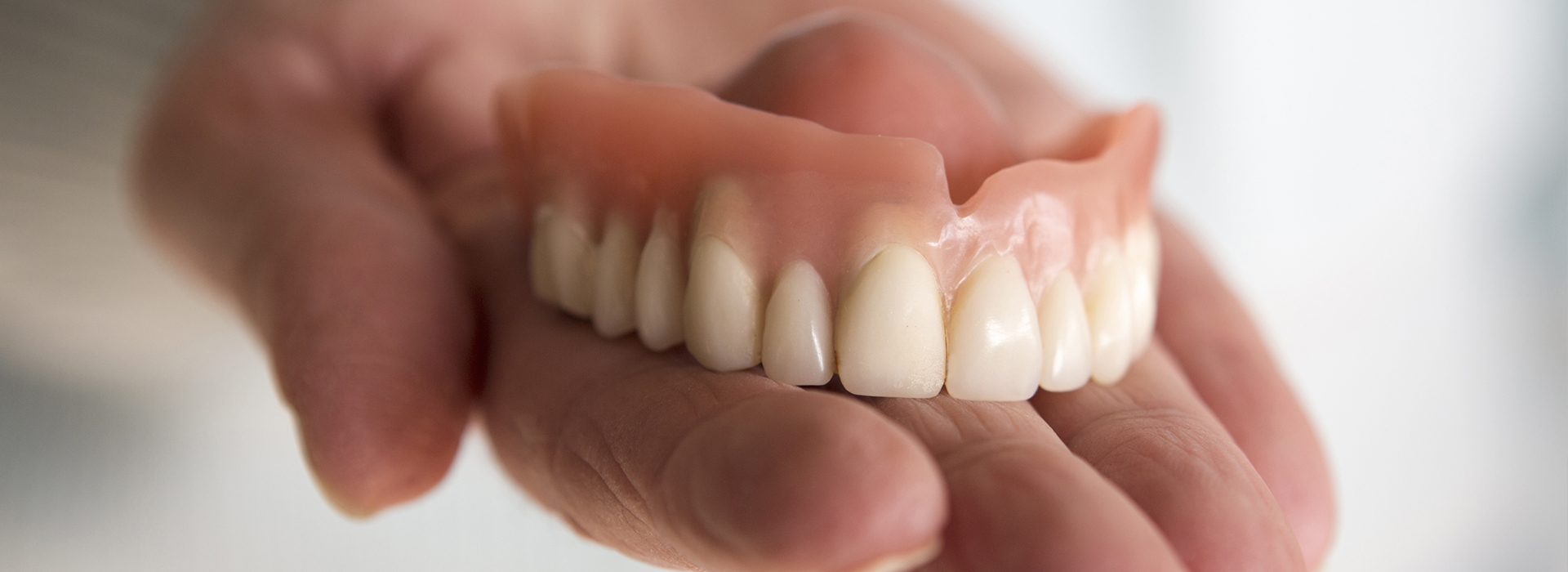 The image shows a person holding a set of dentures, which are white and appear to be in the shape of human teeth.