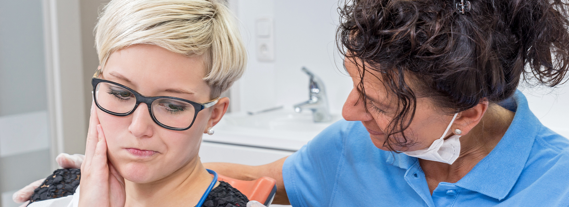 The image shows a woman in a dental chair receiving dental care from a professional, with a focus on the interaction between them.