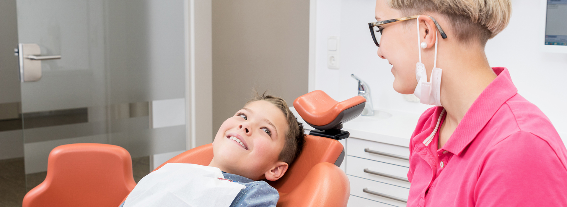 A dental professional and a child in a dental chair, with the professional smiling at the camera.