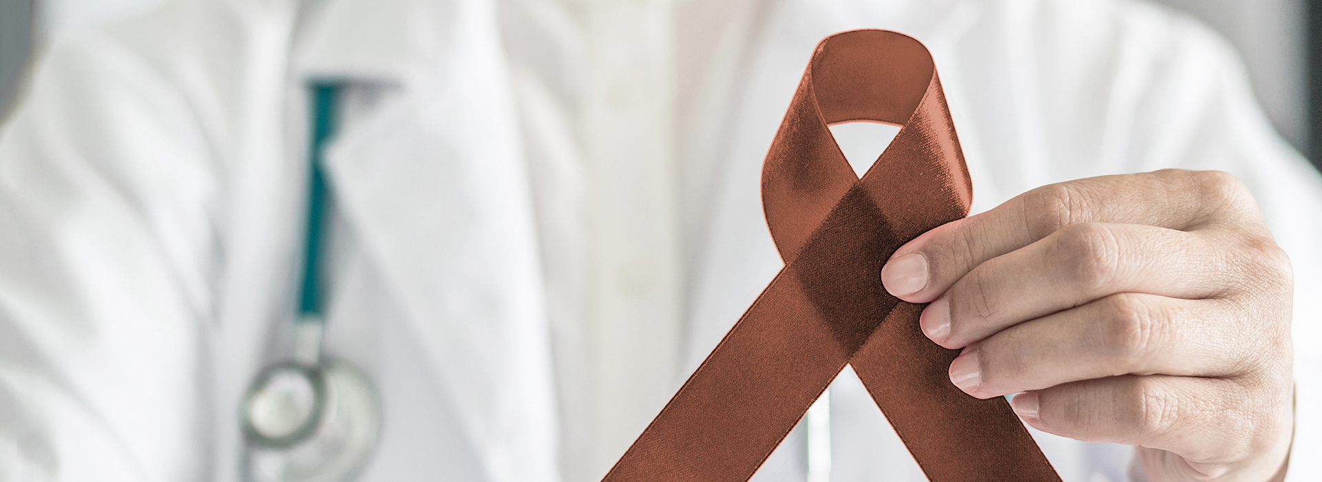 The image shows a hand holding a red ribbon with the shape of an organ, possibly representing awareness for a specific health issue.