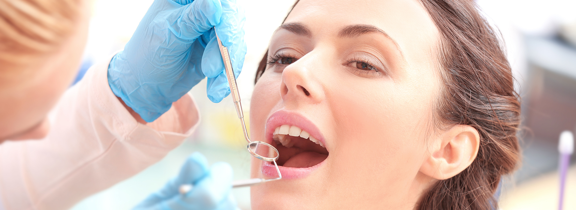 The image shows a woman receiving dental care, with a dental professional using a drill to work on her teeth.