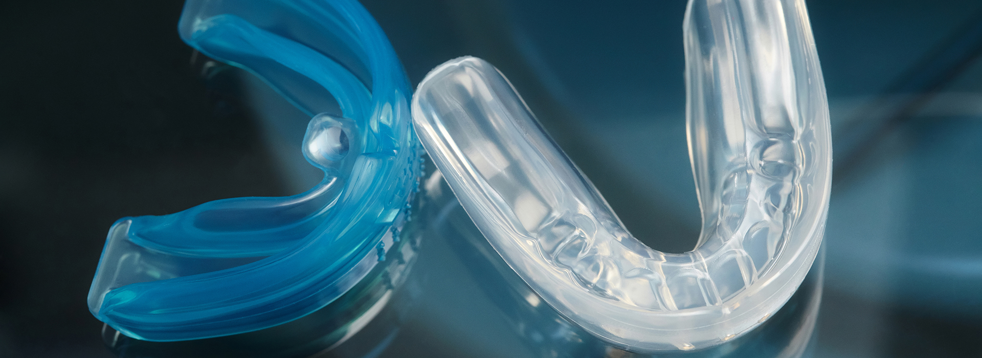 The image shows a close-up of two transparent plastic braces with blue accents, one placed on top of the other against a blurred background.