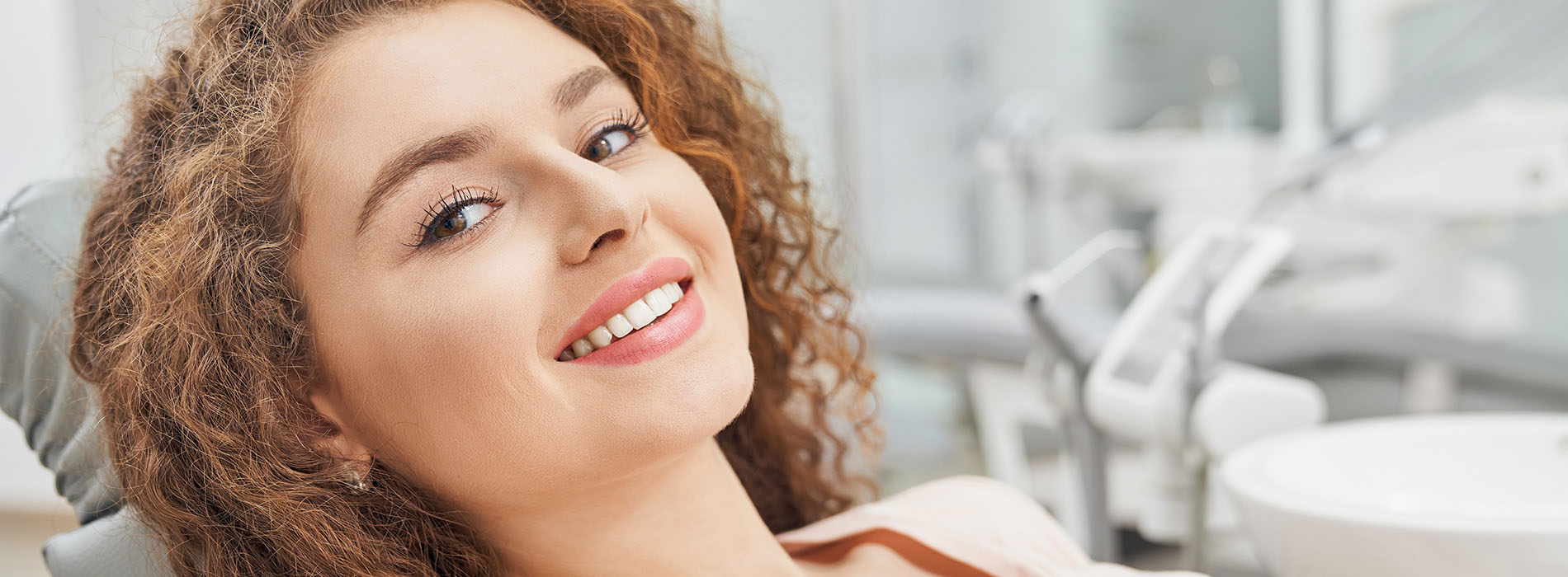 The image is a photograph of a smiling person in a dental office, sitting in a dentist s chair with their head resting on the chair s backrest.