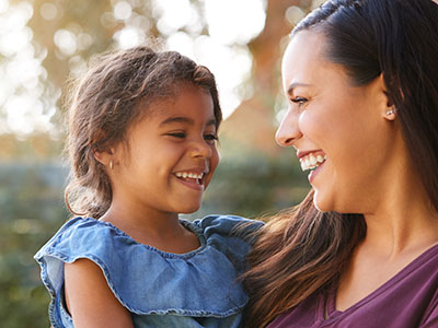 A woman and a young girl sharing a joyful moment, with the woman smiling broadly at the camera.