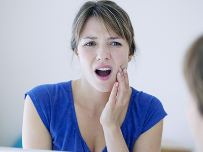 A woman with surprised expression, holding her mouth and looking at a reflection in the mirror.