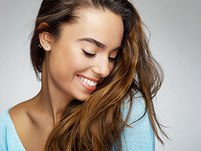 A smiling woman with long hair, wearing a light blue top, against a neutral background.