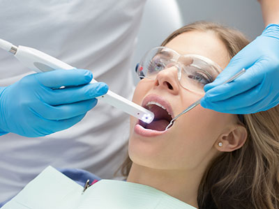 This image shows a person with their mouth open wide, receiving dental care from a professional who appears to be using an electric toothbrush for cleaning purposes.
