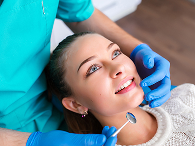 A dental professional performing a dental procedure on a patient, with the patient smiling and wearing blue gloves.