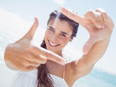 A woman with a radiant smile holds up her hand, framing the image with her fingers.