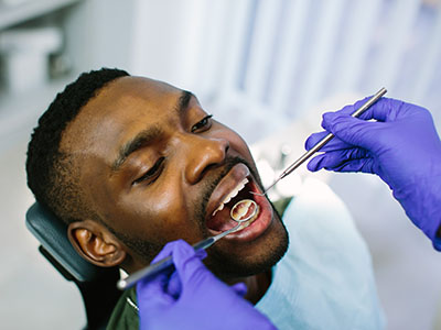 The image shows a person in a dental chair receiving dental treatment, with a dentist performing the procedure using specialized tools.